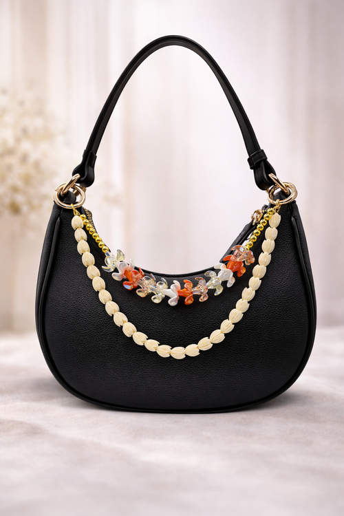 Kenna charm in Puakenikeni displayed on a black handbag with gold-tone hardware and floral-inspired beads