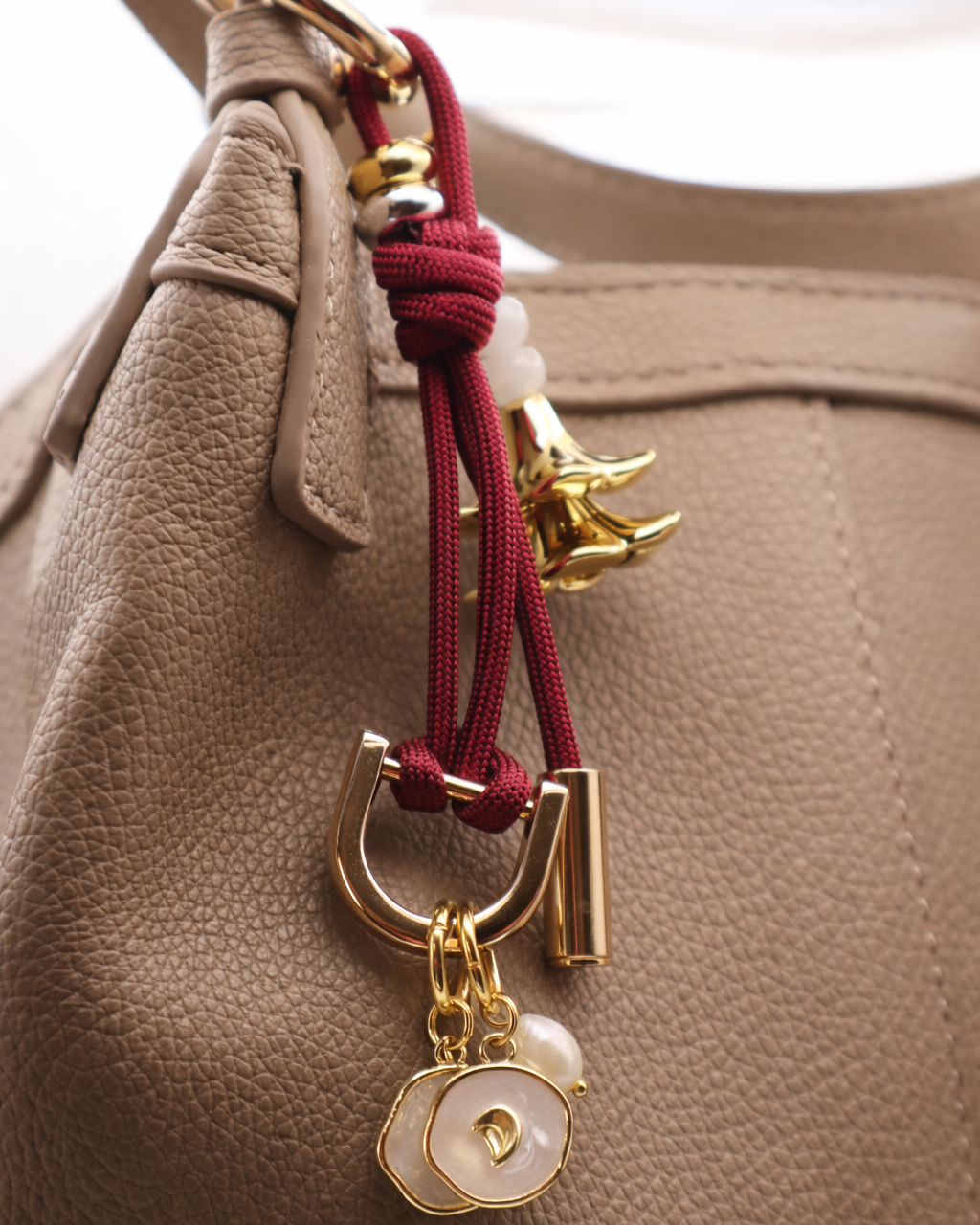 Decorative keychain with gold accents and red cord on a beige handbag.